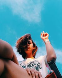 Beautiful young woman sitting on shore against blue sky