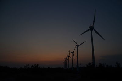 Silhouette wind turbines against sky during sunset