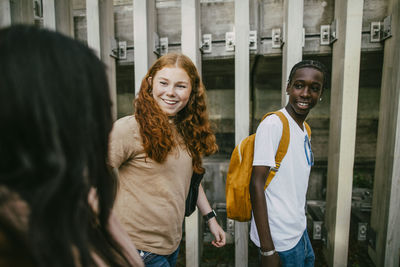 Smiling male and female teenagers talking with friend while walking near fence