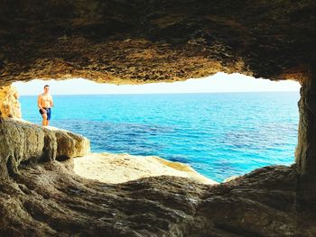 Rear view of woman standing on rock by sea