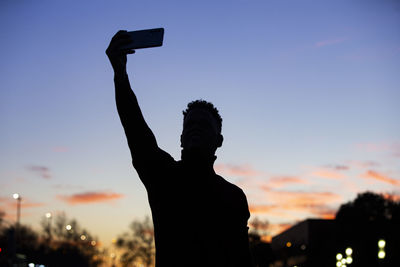 Low angle view of silhouette man with arms raised against sky during sunset