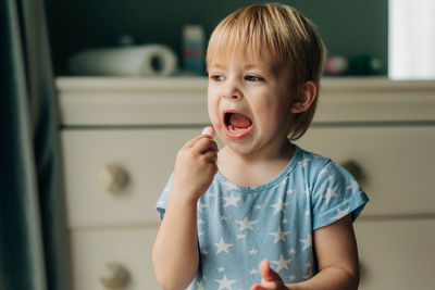 Little funny girl paints her lips with pink lipstick.