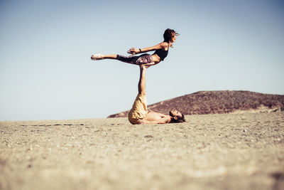 Couple exercising on beach against clear sky