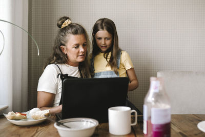 Mother and daughter using laptop at dining table