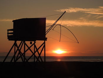 Silhouette hut by sea against sky during sunset