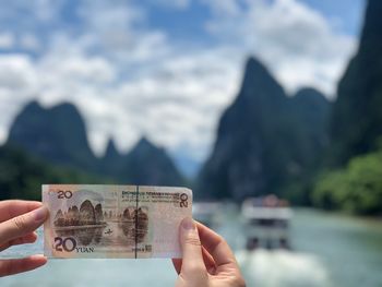 Cropped hands holding paper currency against mountains