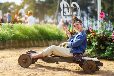Portrait of woman gesturing peace sign while sitting on cart in park