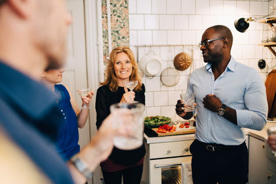 Mature friends talking while enjoying drinks in party at home