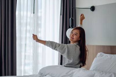 Portrait of young woman using phone while sitting on bed at home