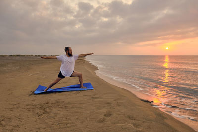 Man stands on blue exercise man doing virabhadrasana two pose. man practices warrior two asana
