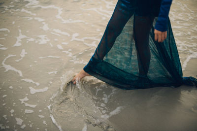 Low section of woman playing with water at beach