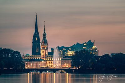 Illuminated buildings by river against sky in city