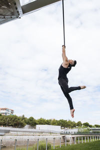 Low angle of fit male gymnast hanging on aerial straps during training in park