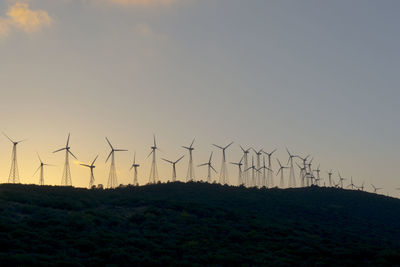 Wind turbines on field against sky during sunset