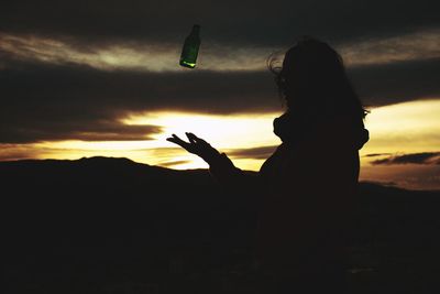 Silhouette woman holding smart phone against sky during sunset