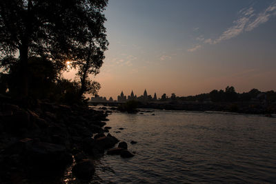 Silhouette of trees by river during sunset