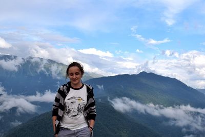 Smiling young woman standing on mountain against sky