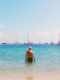 Rear view of shirtless man in sea against sky on sunny day