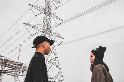 Low angle view of man and electricity pylon against sky