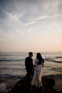 Rear view of couple at beach against sky during sunset