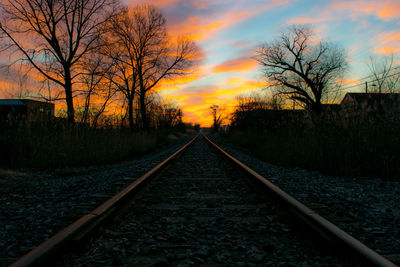 Diminishing perspective of railroad track against sky during sunset