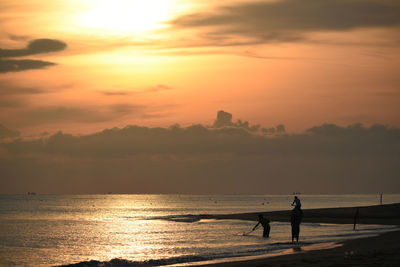 Silhouette people on sea against sky during sunset