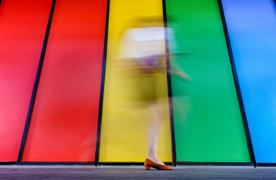 Low section of woman walking on multi colored wall