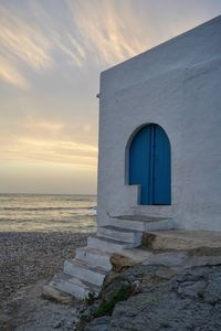 Built structure on beach by sea against sky during sunset