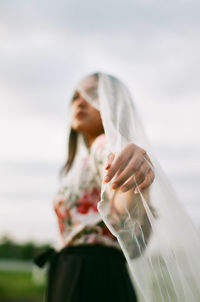 Low angle view of woman wearing scarf while standing against sky