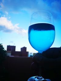 Close-up of hand holding drink against blue sky