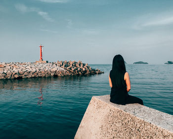 Rear view of woman standing on rock by sea against sky