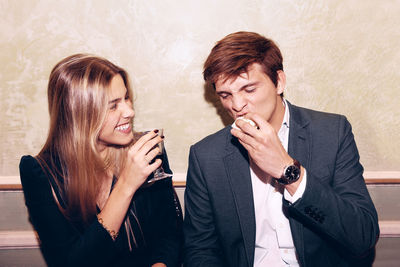 Positive woman with wineglass looking at man eating delicious food while sitting together near wall during dinner in modern restaurant