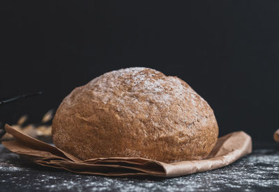 Round white bread on a paper bag on a black table.