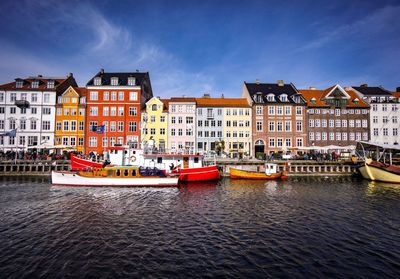 Boats in canal by buildings against sky in city