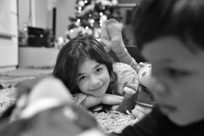 Portrait of girl lying on carpet with brother in foreground at home