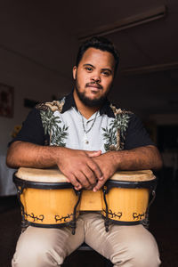 Black male musician in casual clothes sitting on chair with drums while smiling and looking at camera