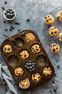 A muffin tin filled with blueberry muffins, blueberries and brown sugar.
