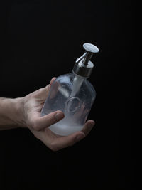 Midsection of person holding bottle against black background