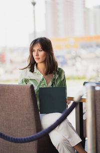 Portrait of a beautiful woman in fashionable clothes holding a book with a blank green cover.