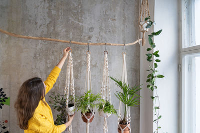 Side view of woman hanging plants at home