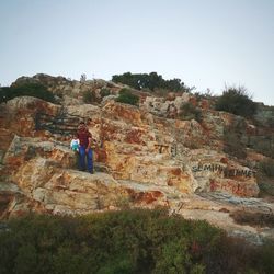 Rear view of man standing on rock against clear sky