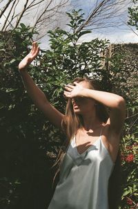 Young woman shielding eyes while standing against plants