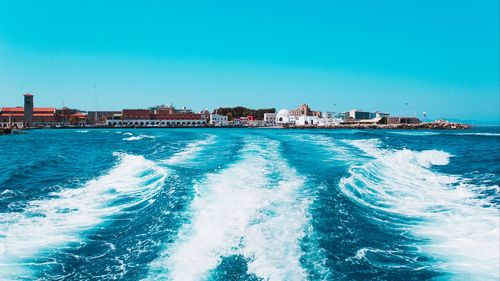 Scenic view of sea against buildings against clear blue sky