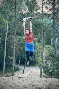 Full length of playful young woman on rope swing in forest