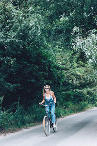 Full length of woman riding bicycle on road in forest