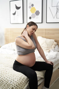 Tired pregnant woman sitting on bed