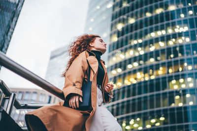 Side view of young woman standing against modern buildings