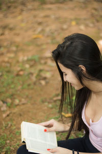 Smiling woman reading book while sitting outdoors