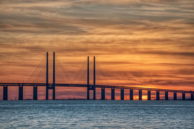 Bridge over calm sea against orange sky