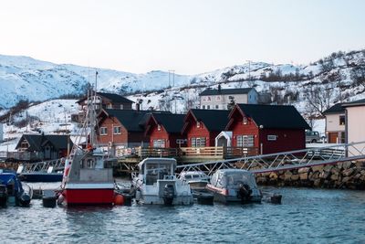 Boats moored on lake by houses against snowcapped mountains